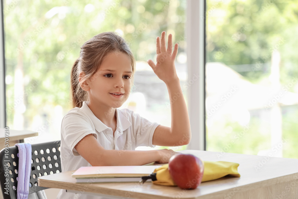Little schoolgirl raising hand at desk in classroom Little schoolgirl raising hand at desk in classroom
