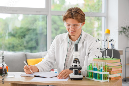 Male student in lab coat with notebook and microscope studying at home