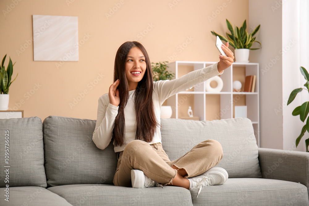 Young Asian woman with mobile phone taking selfie on sofa at home Young Asian woman with mobile phone taking selfie on sofa at home