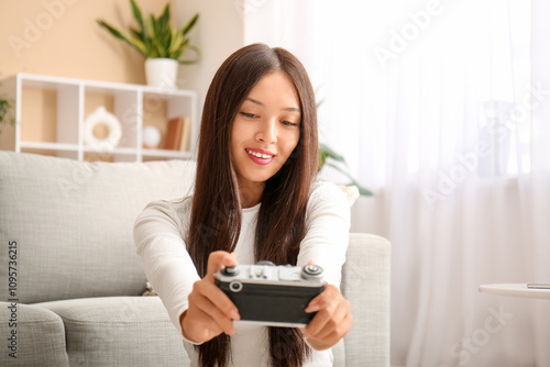 Young Asian woman with photo camera taking selfie at home