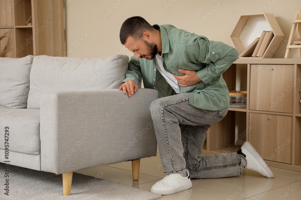 Young man suffering from heart attack near sofa at home Young man suffering from heart attack near sofa at home