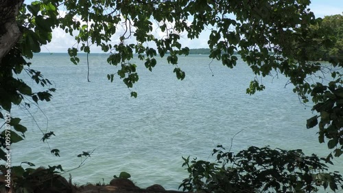 Beautiful coastal view with blue waters and rock islands framed by tree leaves photo