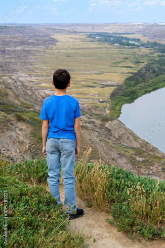 Boy is stanfing on the top of the hill and looking at the river. Red deer river, Drumheller, Alberta, Canada. photo