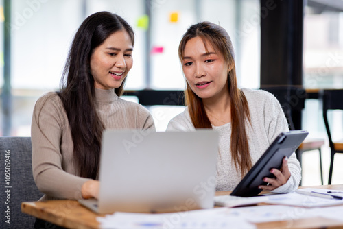 Two asian confident business people point to graphs and charts to analyze market data, balance sheet, account, net profit to plan new sales strategies to increase production capacity. 