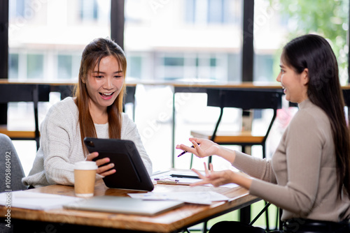 Two asian confident business people point to graphs and charts to analyze market data, balance sheet, account, net profit to plan new sales strategies to increase production capacity.	
