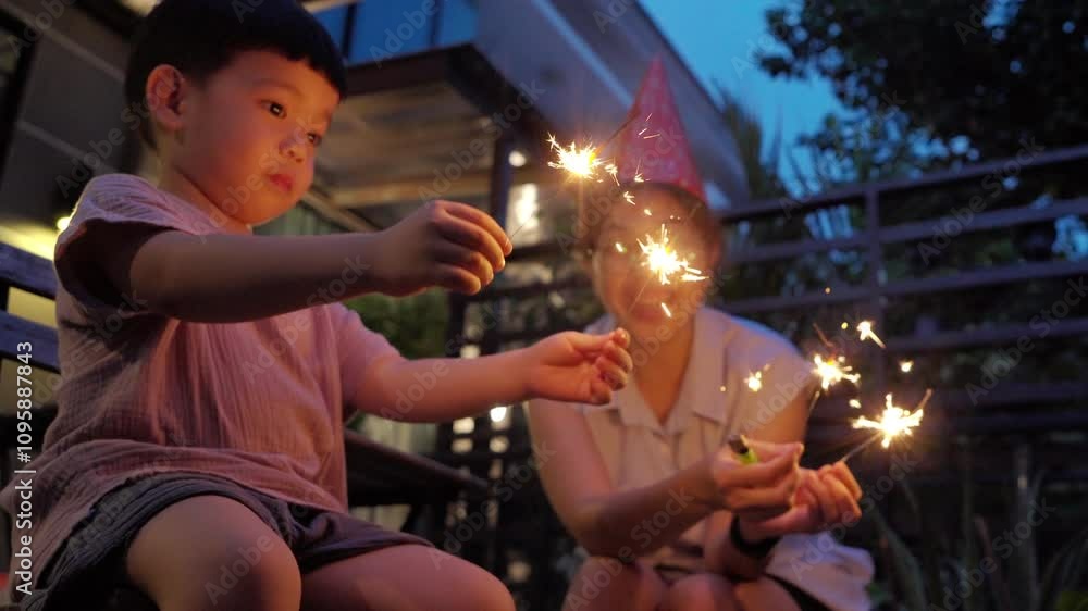 Happy Asian Mother and little son holding sparklers outdoors at night, celebrating a special occasion, with joyful expressions and festive ambiance. Birthday and New year celebration.