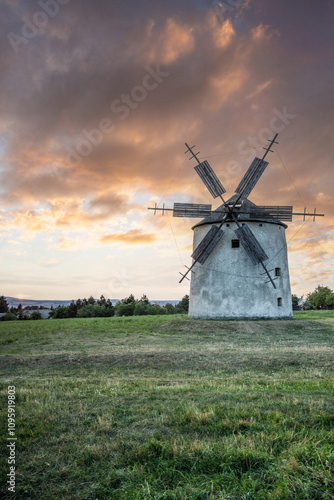 Windmill with wooden wings in a landscape setting. Fields, meadows and flowers appear in the sunset. Landscape shot in nature with a mill. historically untypical for the Balaton region in Hungary