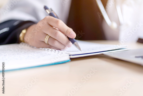 Closeup and crop hands of Muslim student in Abaya niqab traditional clothes holding a pen writing on note book in classroom.