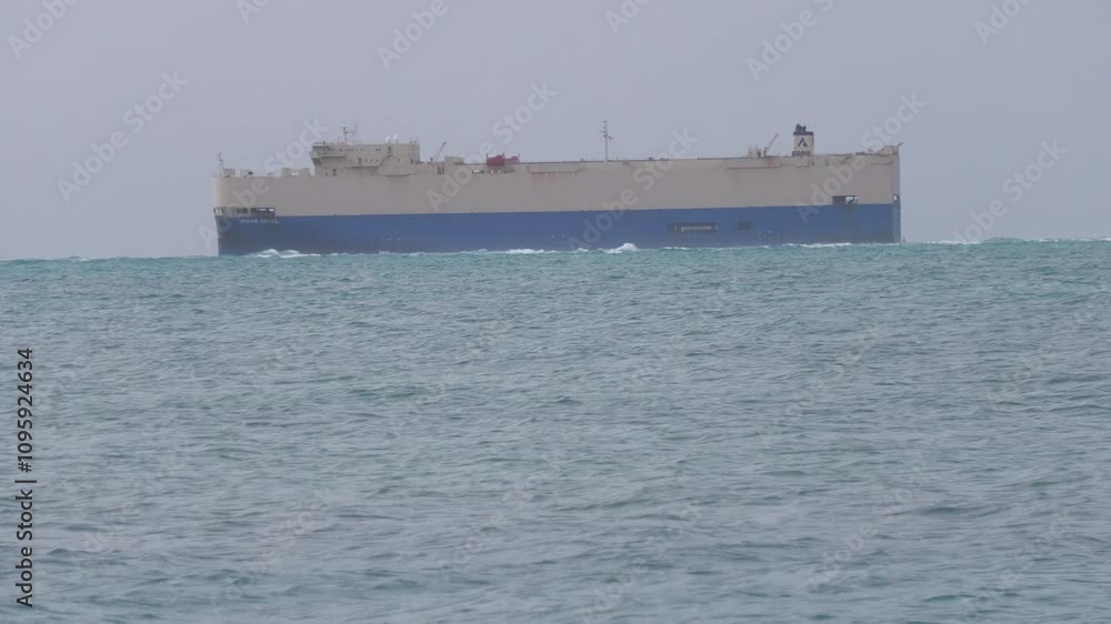 Medium wide shot of a cargo ship navigating the waters, tropical island Medium wide shot of a cargo ship navigating the waters, tropical island
