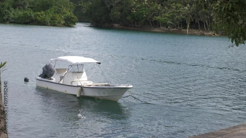 Flowing water of a lagoon with a white boat tied to a rope floating in the water, handheld foootage