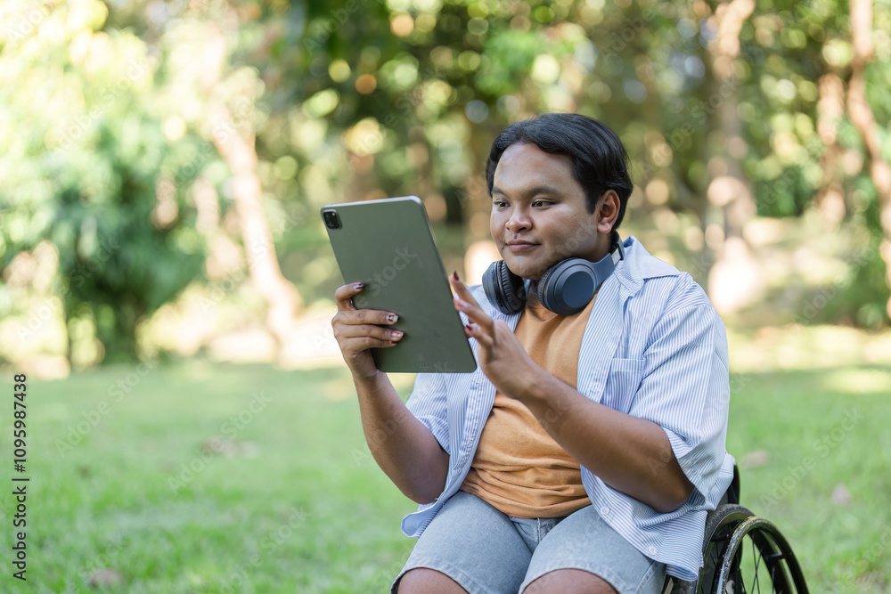 Young Man in Wheelchair Working Outdoors with Tablet and Headphones in a Garden Setting Young Man in Wheelchair Working Outdoors with Tablet and Headphones in a Garden Setting