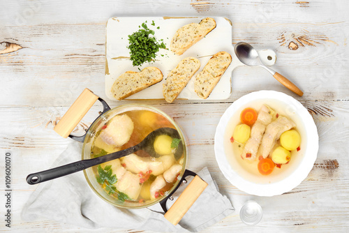 Delicious homemade fish soup with fresh herbs and sliced bread on a wooden table photo