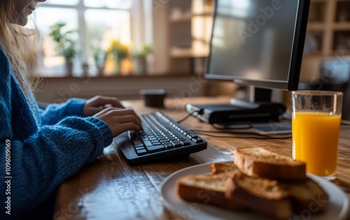 A Young woman working from home, wearing a blue sweater, a black computer and...