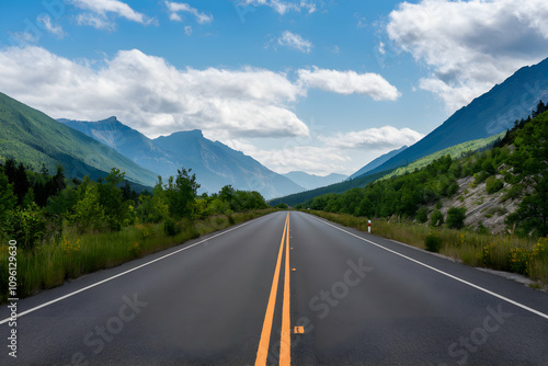 Scenic road lined with green mountains, leading towards clear blue sky and clouds. photo