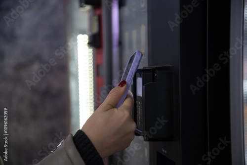 Close-up view of woman paying for purchase at free standing coffee vending machine using smartphone. Soft focus. Contactless and cashless payment theme.