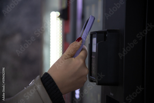 Close-up view of woman paying for purchase at free standing coffee vending machine using smartphone. Soft focus. Contactless and cashless payment theme.