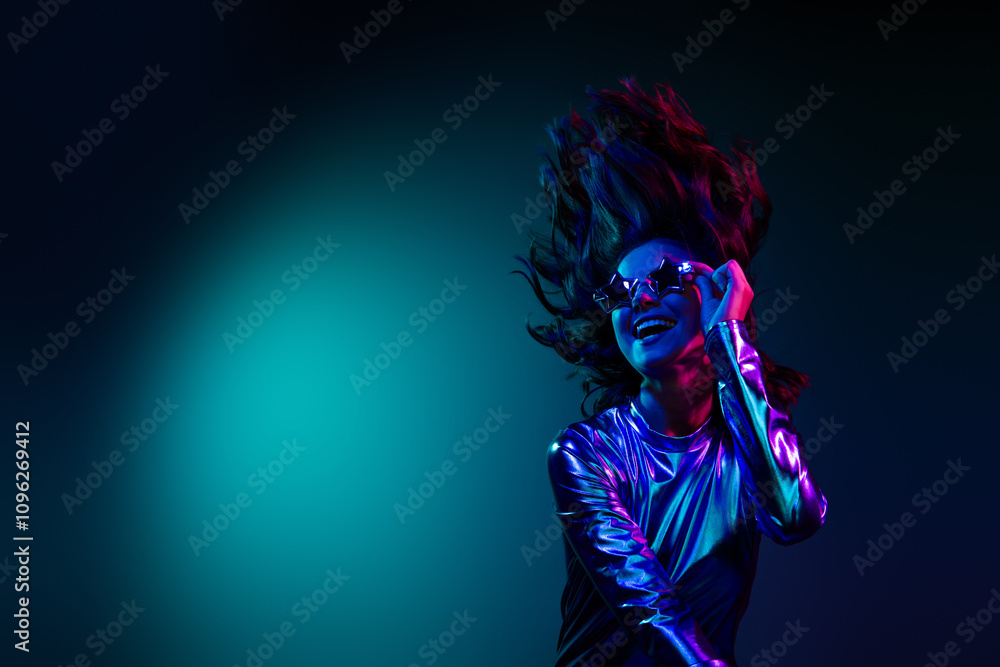 Photo of gorgeous young girl touch sunglass empty space wear shiny dress neon light dark blue background Photo of gorgeous young girl touch sunglass empty space wear shiny dress neon light dark blue background