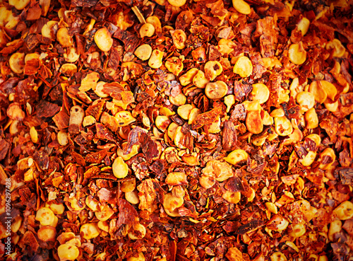 Background or backdrop of top closeup view of dried red hot chili pepper flakes with seeds cultivated for pungency used as ingredient in culinary as spice or seasoning to add heat for capsaicin 