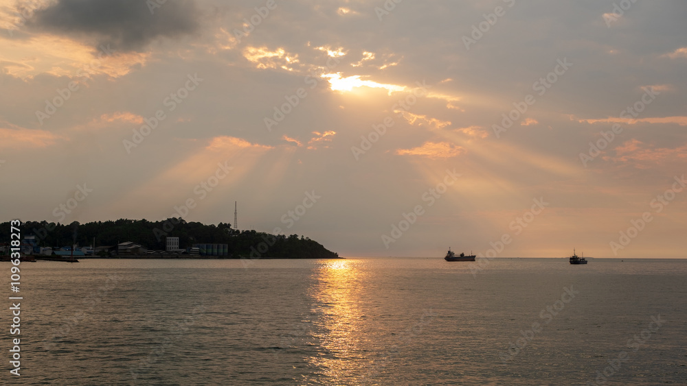 Dramatic view of an industrial port with a cargo ship sailing with the afternoon sun shining through the clouds. Industrial background wallpaper concept Dramatic view of an industrial port with a cargo ship sailing with the afternoon sun shining through the clouds. Industrial background wallpaper concept