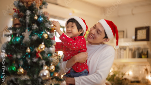 Happy family preparing New Year winter holidays celebration. Smiling young asian father and son enjoy decorating ornament on christmas tree create festive mood party atmosphere at home. slow motion. 