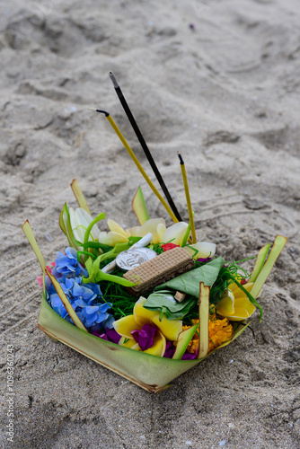 Canang Sari Balinese Offering or Sacrifice Basket with Incense and Flowers in the Sand on Kuta Beach, Bali photo