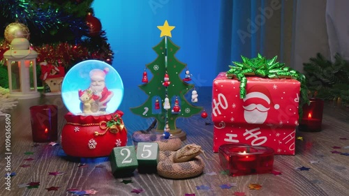 Snake - Symbol of the Year 2025 in the Chinese Lunar Calendar. Festive Christmas Gift Box, Christmas Tree, Glass Snow Globe with Santa Claus, Red Candles, and a Calendar Marked with the Number 25.