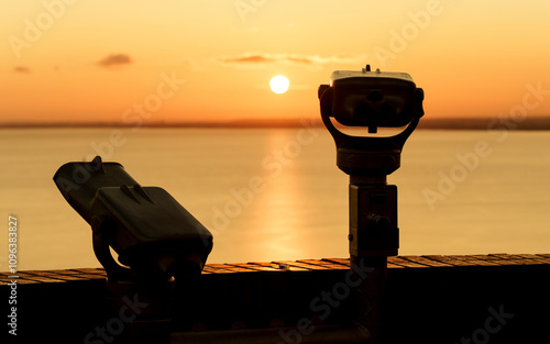 Binoculars on the terrace of Tihany Abbey. An amazing sunrise in the background, with the sun painting a golden line across Lake Balaton.