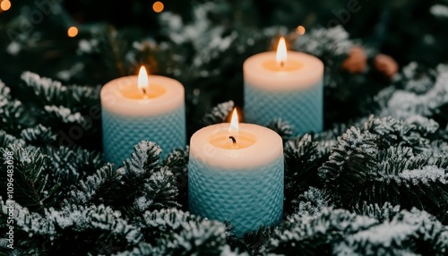 Three light blue candles burning amidst snowy evergreen branches.