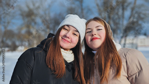 Two happy schoolgirls in winter attire posing together in a snowy park on a sunny winter day photo