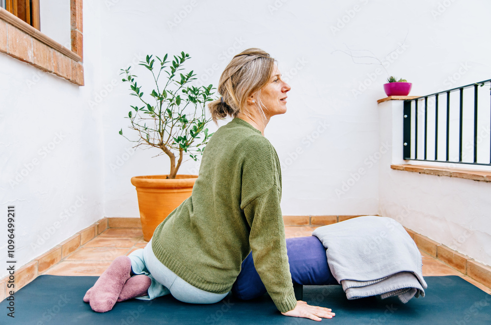 © Cristina - Woman in a warm outfit practising restorative yoga on a cosy outdoor terrace