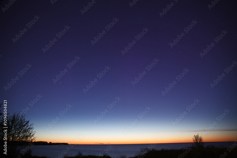 Night clear sky view with starts and late sunset on horizon, sea shore