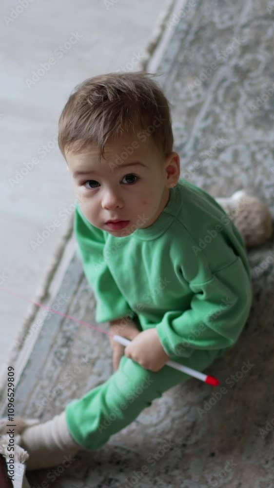 Adorable baby boy sitting on the floor looking up with surprise. Lovely toddler holding the toy for a cat. Vertical video Adorable baby boy sitting on the floor looking up with surprise. Lovely toddler holding the toy for a cat. Vertical video