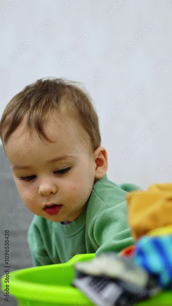 Baby boy taking the dirty clothes out of the washbowl. One year old kid playing in the house. Vertical video Baby boy taking the dirty clothes out of the washbowl. One year old kid playing in the house. Vertical video