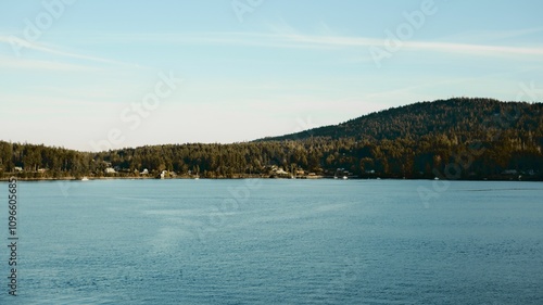 Serene lake with forested hill under blue sky