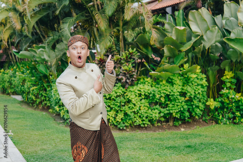 Surprised young Asian man in traditional Javanese beskap and batik presenting the copy space upside. photo