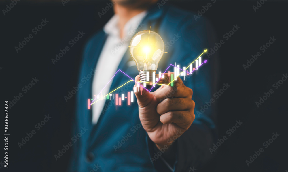 A businessman holding a glowing light bulb with financial graphs and upward trends, symbolizing innovation, success, and business growth.