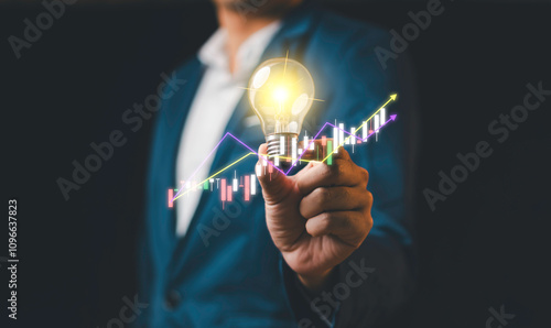 Obraz na płótnie A businessman holding a glowing light bulb with financial graphs and upward trends, symbolizing innovation, success, and business growth. w salonie