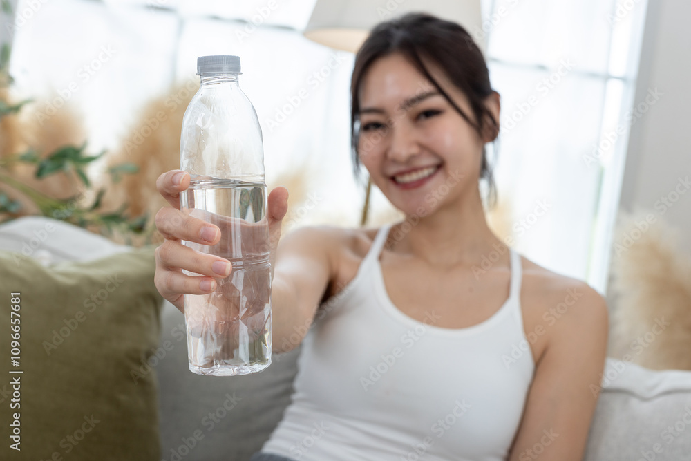 Close up water bottle. Asian young female sporty drinking water sitting on sofa in living room while exercising. stay hydrated per day. Drinking water makes you feel good. Close up water bottle. Asian young female sporty drinking water sitting on sofa in living room while exercising. stay hydrated per day. Drinking water makes you feel good.