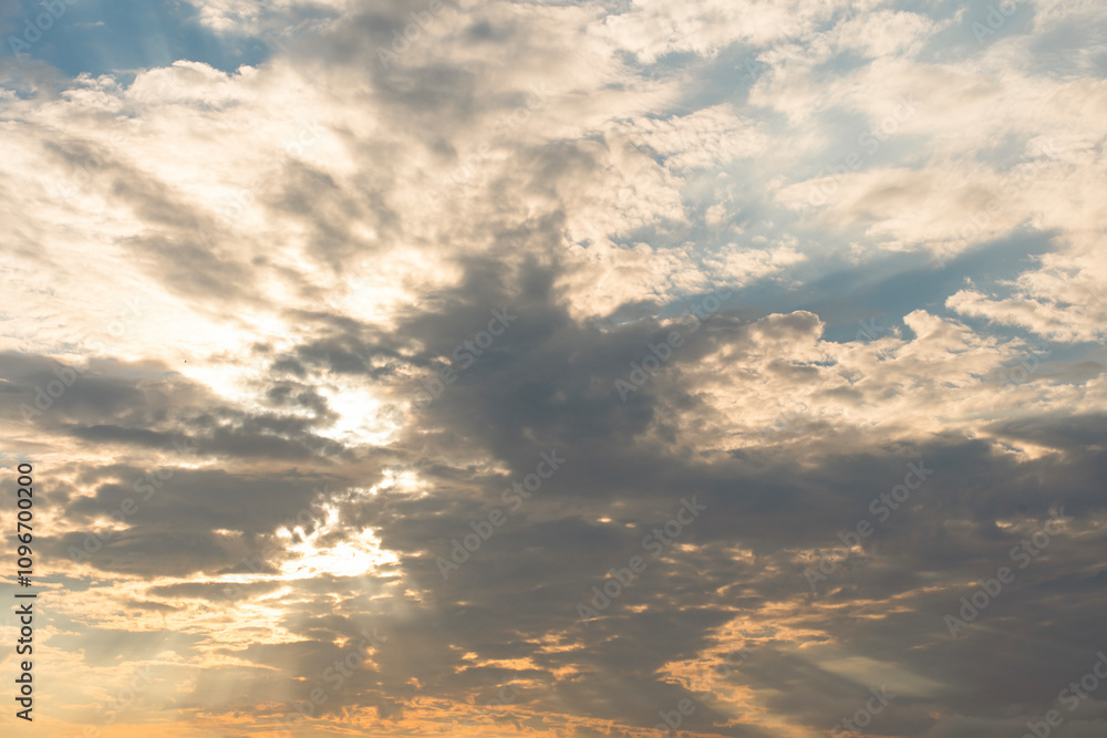 Fototapeta premium Clouds illuminate the sky with rays of sunlight during a serene sunset over a tranquil horizon