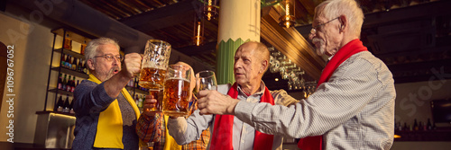 Elderly people, men in colorful red and yellow scarves meeting at bar, pub, clinking beer mugs and celebrating victory of favorite soccer team. Sport fans, elderly lifestyle, leisure activity concept photo