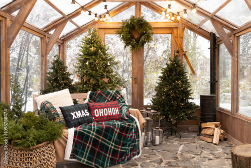 A festive sunroom with a cozy bench, Christmas trees, and holiday decor, offering a warm and inviting view of a snowy winter wonderland.