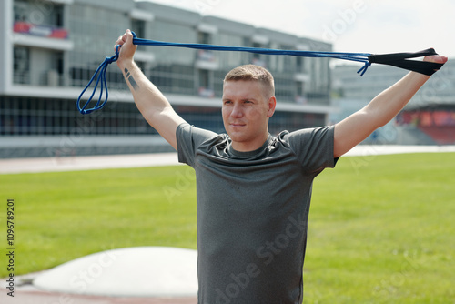 Man using resistance band for workout on outdoor track. Multi-story buildings in background giving urban feel. Focused expression and posture indicate dedication photo