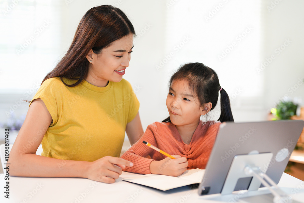 An adorable young Asian girl enjoys learning English online on a laptop with a female teacher, sitting at a table together. An adorable young Asian girl enjoys learning English online on a laptop with a female teacher, sitting at a table together.