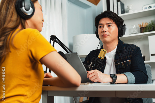 Smiling radio influencer host holding tablet wearing headphones interview woman speaker social media online live streaming channel with talking to share link at morning at studio record. Infobahn.