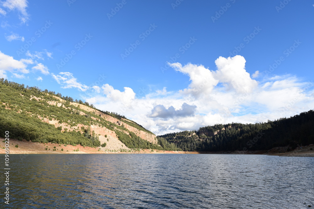 This image showcases a tranquil lake surrounded by lush greenery and hills in the Middle Atlas Mountains of Morocco. The serene water reflects the bright blue sky scattered with fluffy white clouds. This image showcases a tranquil lake surrounded by lush greenery and hills in the Middle Atlas Mountains of Morocco. The serene water reflects the bright blue sky scattered with fluffy white clouds.