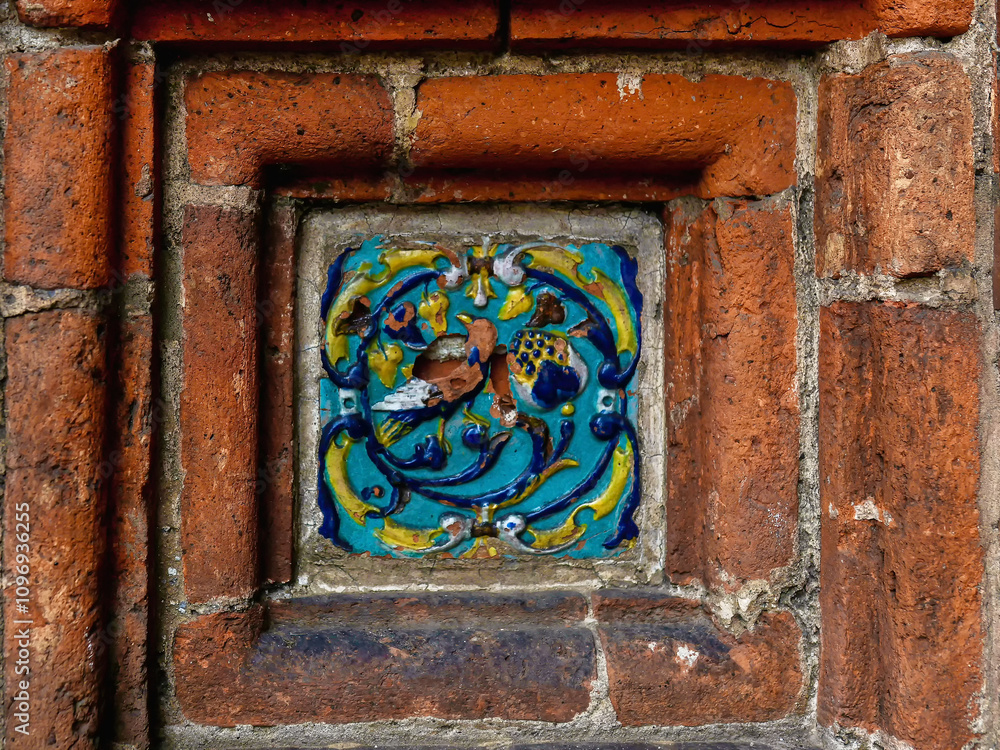 Ancient tiles in the red brick wall close up. Tile on exterior decor. Ancient tiles in the red brick wall close up. Tile on exterior decor.
