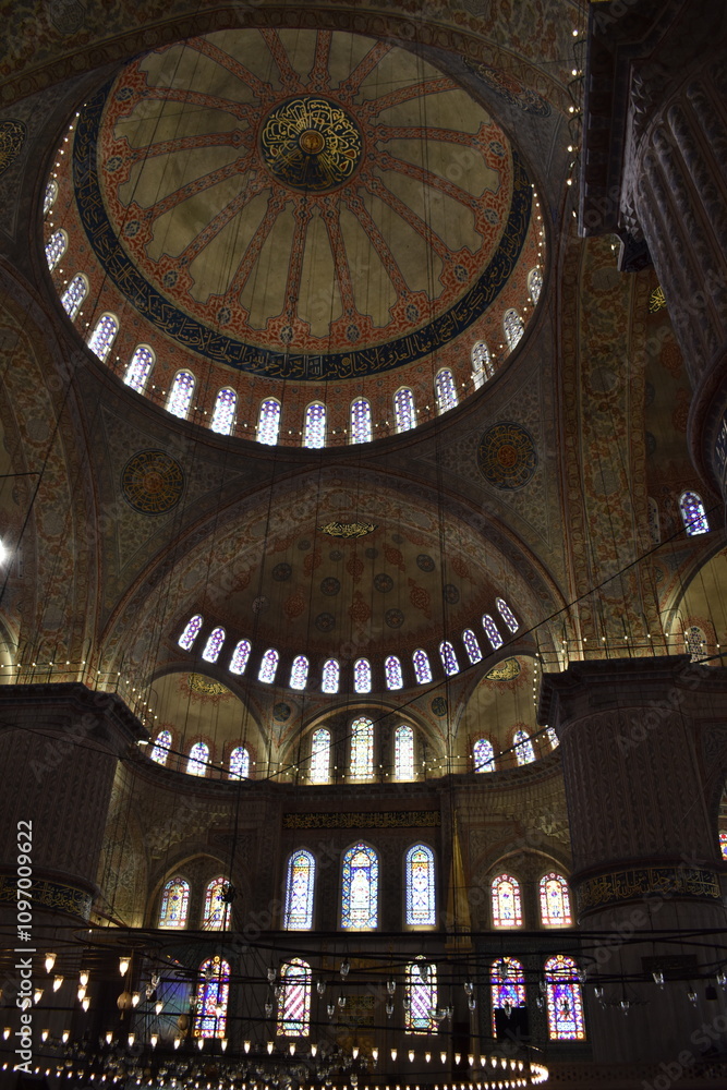 Obraz premium The interior dome of a mosque in Istanbul, adorned with intricate Islamic calligraphy and colorful stained glass windows. The soft lighting enhances the rich patterns and architectural grandeur 