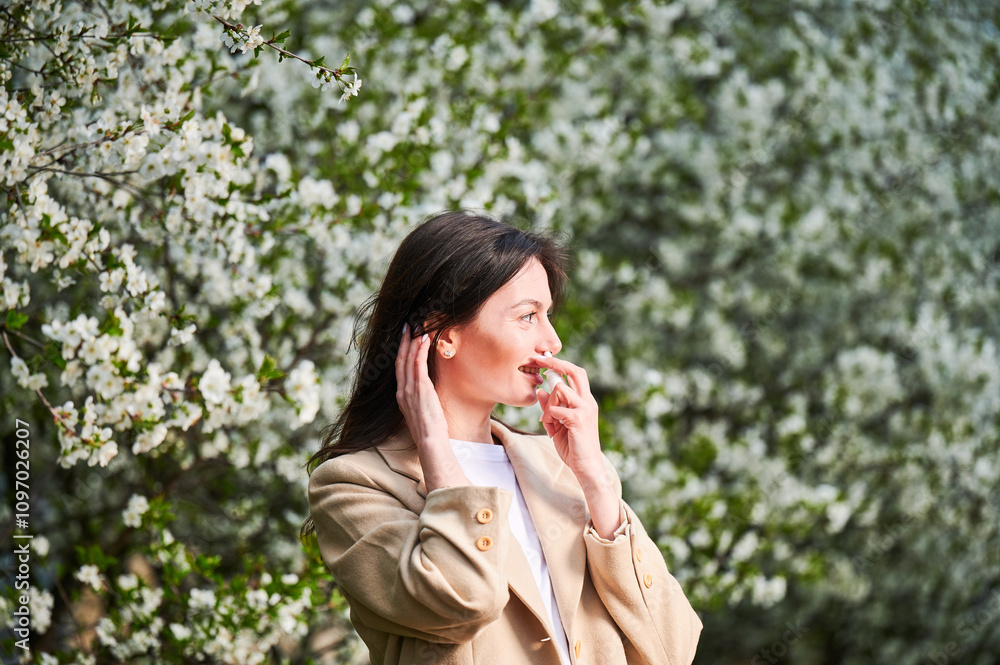 Woman allergic using medical nasal drops, suffering from seasonal allergy at spring in blossoming garden. Young woman treating runny nose in front of blooming tree outdoors. Spring allergy concept. Woman allergic using medical nasal drops, suffering from seasonal allergy at spring in blossoming garden. Young woman treating runny nose in front of blooming tree outdoors. Spring allergy concept.