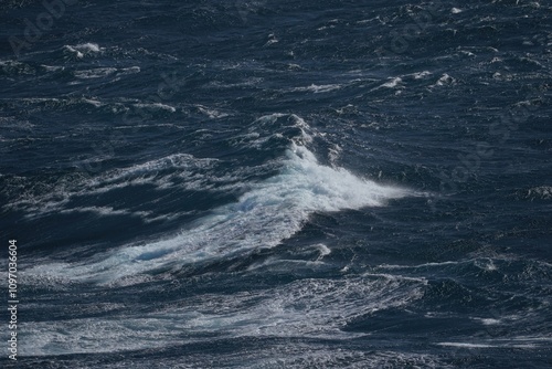 image captures dynamic movement of ocean waves, showcasing deep blue water and frothy white crests. scene evokes sense of power and tranquility in nature