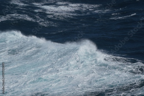 powerful ocean wave crashes against shore, creating misty spray. deep blue water contrasts with white foam, showcasing beauty of nature force